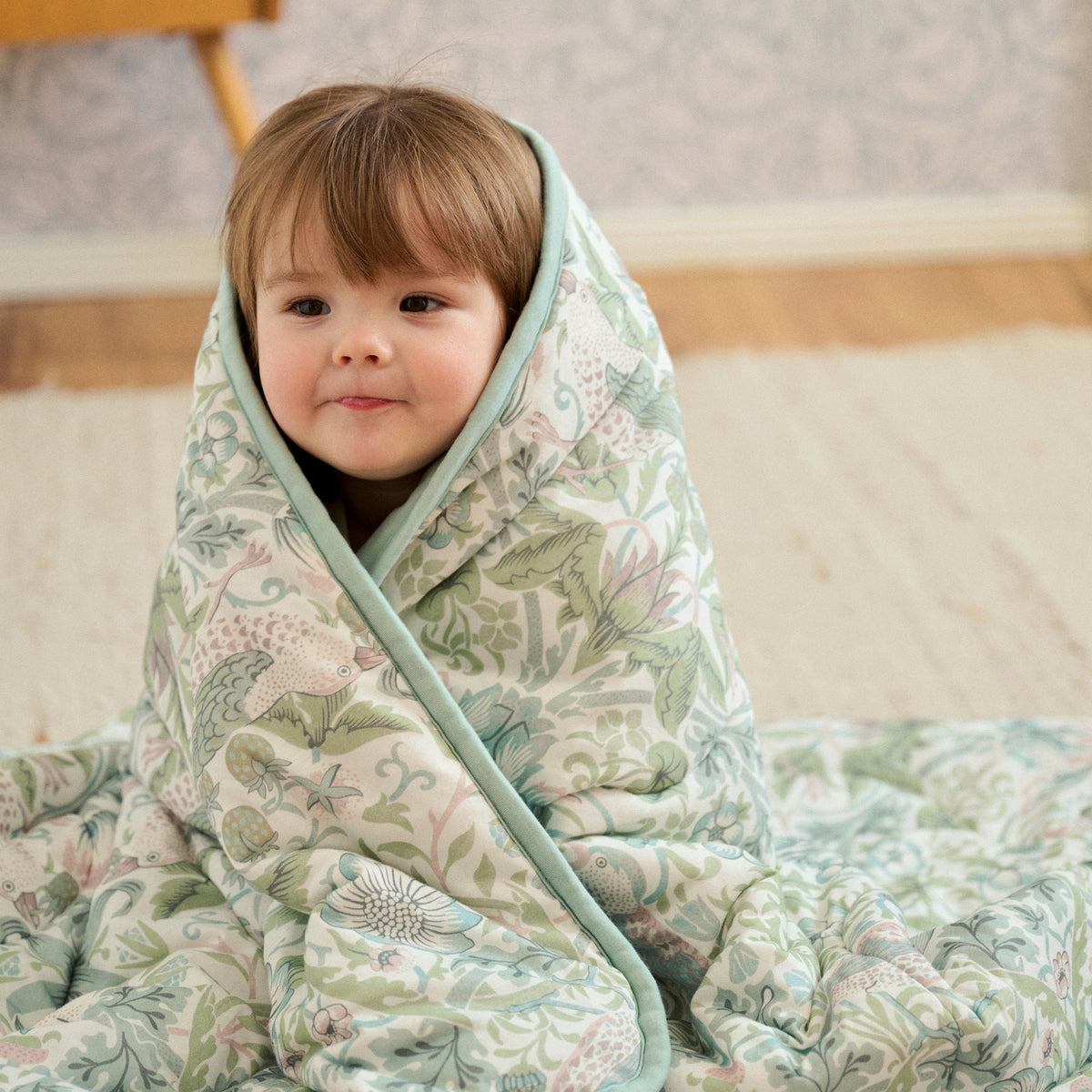 Child wrapped in Strawberry Thief Slate Blue cozy blanket smiling, lifestyle