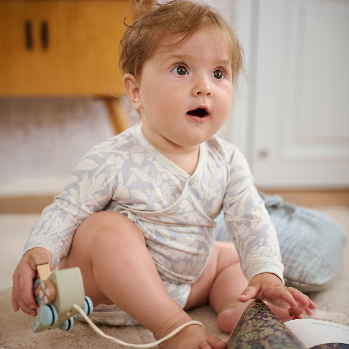 Baby wearing Acorn Slate Blue kimono onesie, playing with toys